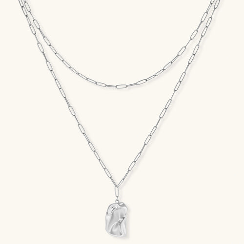 Silver layered necklace with organic flowing pendant in eco-zinc alloy on neutral background, showing adjustable chain design.